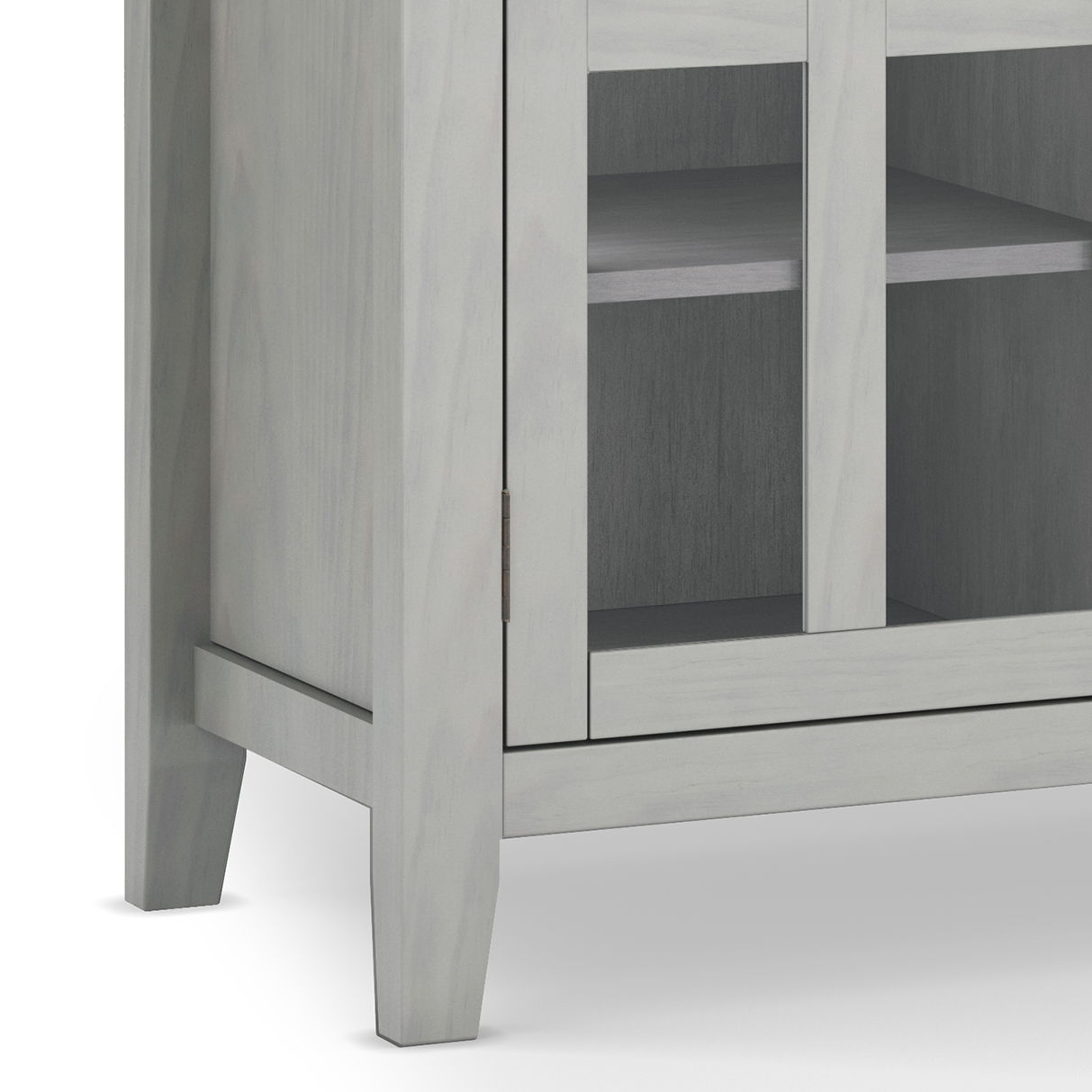 A close-up of the lower corner of the Artisan - Handcrafted, Tall TV Media Stand in light gray shows its legs, glass-front doors, interior shelves, and part of the front panel.