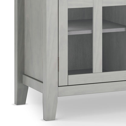 A close-up of the lower corner of the Artisan - Handcrafted, Tall TV Media Stand in light gray shows its legs, glass-front doors, interior shelves, and part of the front panel.