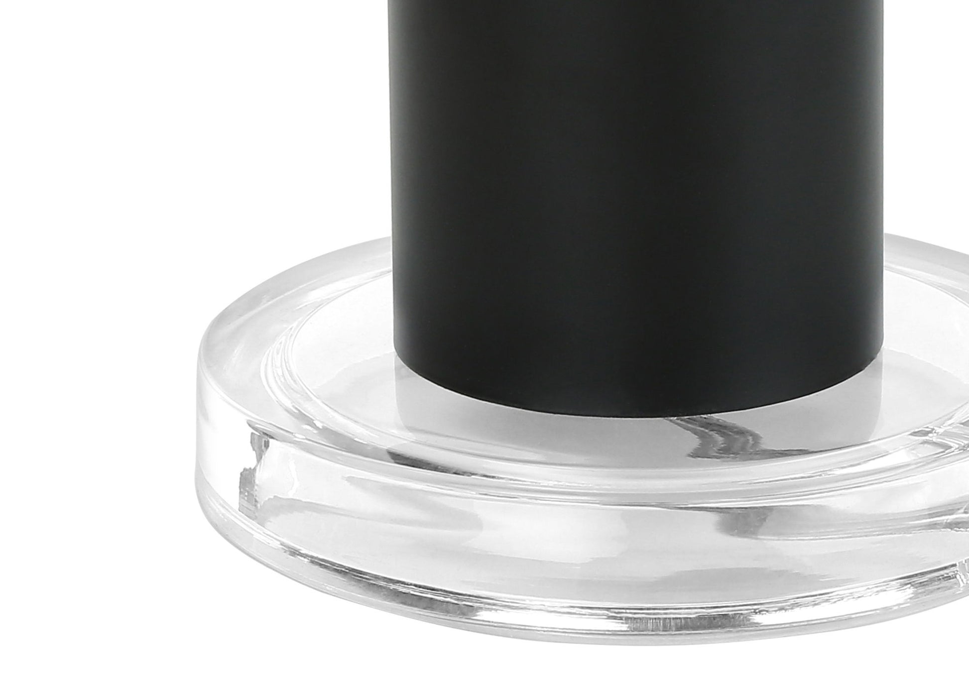 Close-up of the base of a contemporary table lamp in black, resting on a round, transparent glass or acrylic platform against a white background.