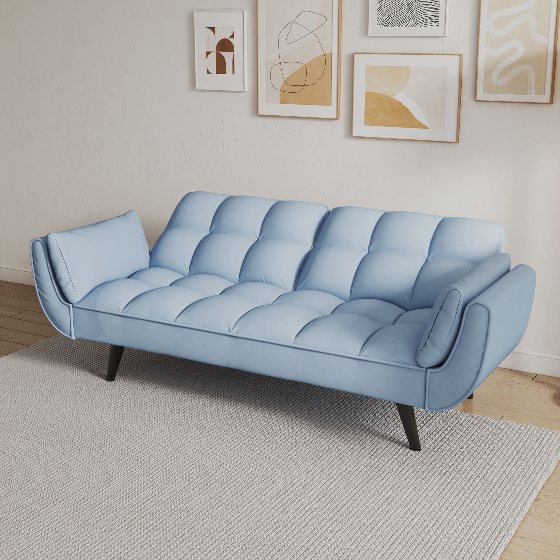 The Sofa Soft, featuring two armrests and cozy throw pillows, is upholstered in light blue and stands on black legs atop a light gray rug in a white-walled room adorned with five abstract art prints.