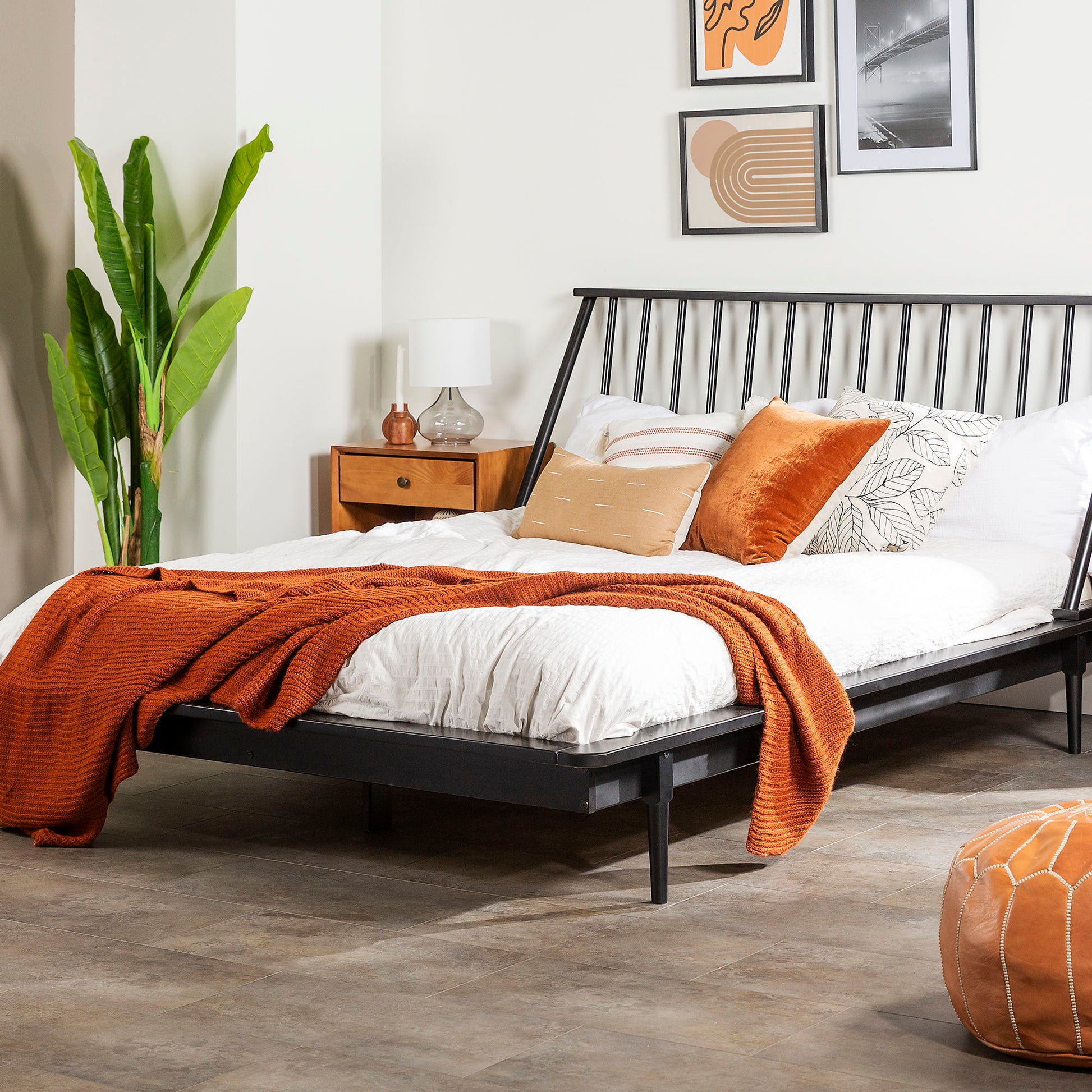 A modern bedroom with the Mid-Century Modern Solid Wood Platform Bed Frame With Spindle Headboard, white bedding, orange throw blanket, assorted pillows, plus a wooden nightstand holding a lamp, green plant, and framed wall art for a cozy, stylish look.