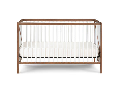 The Pixie Zen 3-in-1 Crib in Walnut features a modern wooden frame with white vertical slats and a white mattress, displayed against a plain white background.