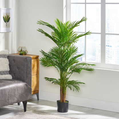 An Artificial Palm Tree in a black pot stands by a gray sofa in a bright, modern room with large windows, light walls, a small wooden dresser, and decorative accents.