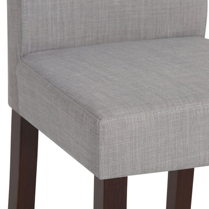 Close-up of the Acadian - Upholstered Parson Dining Chair (Set of 2), featuring a light gray textured fabric seat and backrest with dark wooden legs.