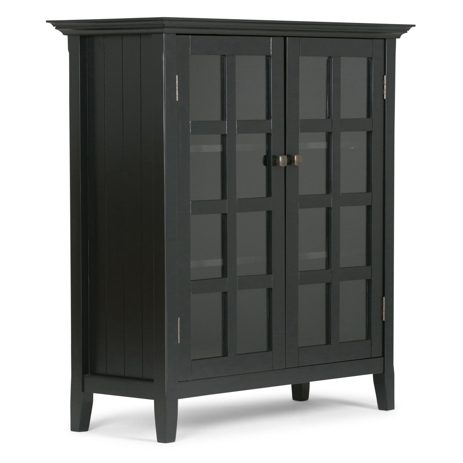 The Acadian - Medium Storage Cabinet is handcrafted from black wood, featuring glass double doors with square grid patterns, vertical side panels, metal center handles, and four short legs.