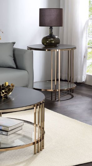 A modern living room showcases the Abisha Sintered Stone Top Round Table with a lamp by a gray sofa, complemented by a matching coffee table holding books and decor, all set on a light rug atop dark wood flooring.