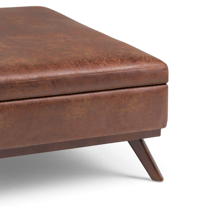 Close-up of the Owen Multifunctional Square Coffee Table Storage Ottoman in brown leather with angled wooden legs and visible stitching, displayed on a white background.