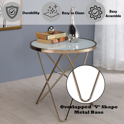 The Valora - Glass Coffee Table, with a round glass top and gold overlapped "V" metal base, sits in a modern room. Icons highlight its durability, easy-to-clean surface, and simple assembly. Decorative objects rest on the table.