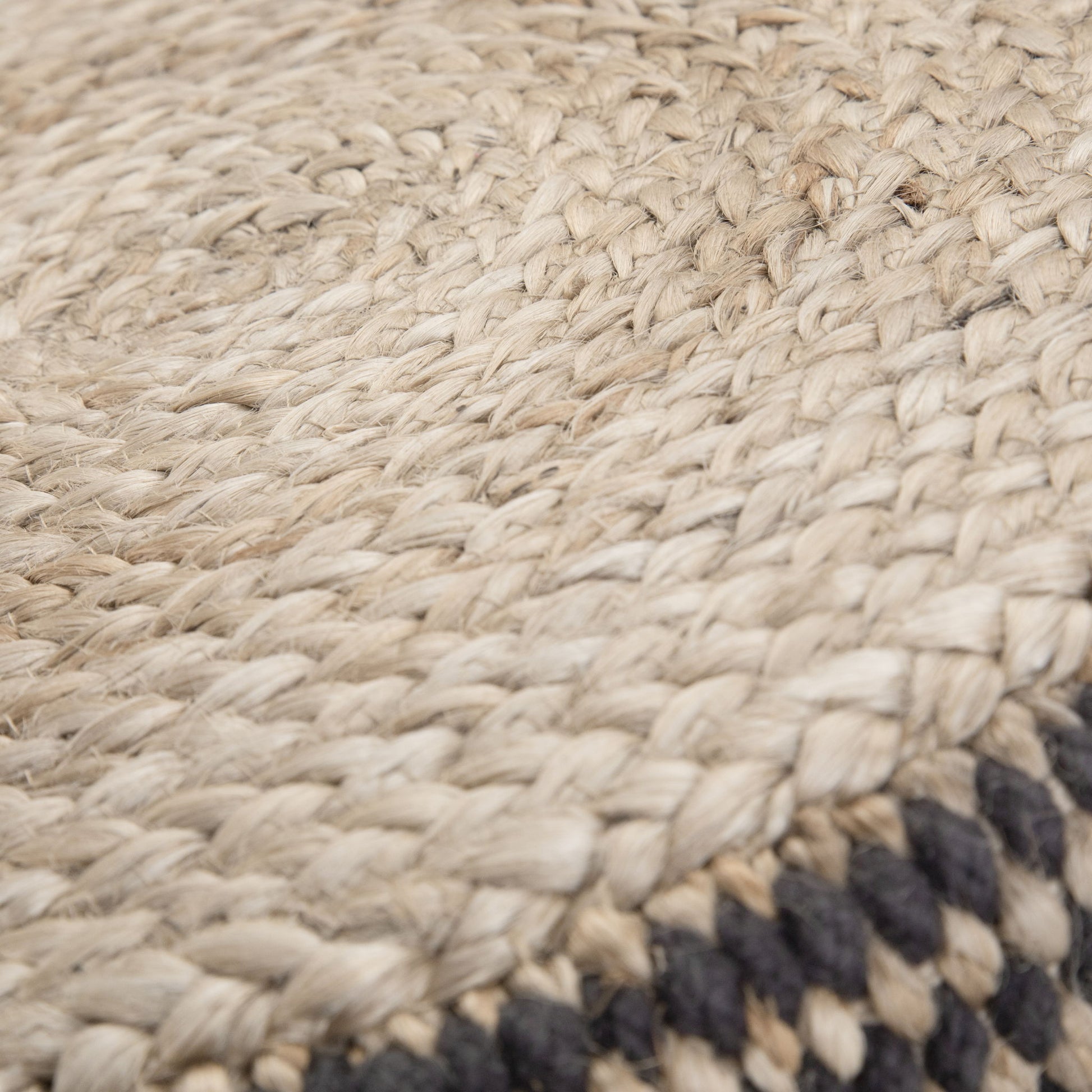 Close-up of the Larissa - Handcrafted Round Braided Pouf, featuring natural beige fibers with a woven pattern and a border of dark-colored strands.