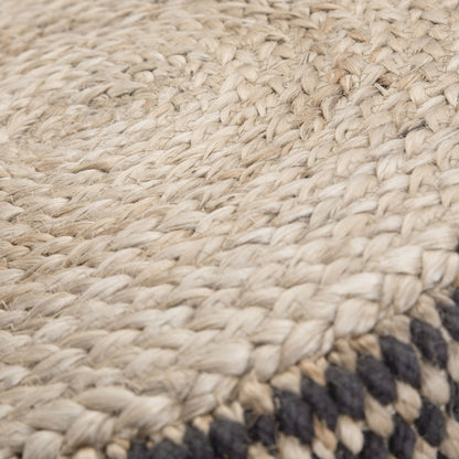 Close-up of the Larissa - Handcrafted Round Braided Pouf, featuring natural beige fibers with a woven pattern and a border of dark-colored strands.