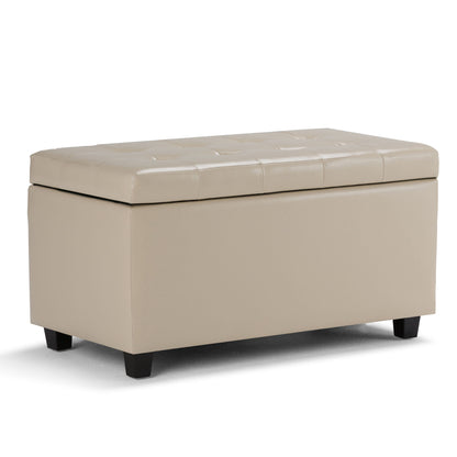 The Cosmopolitan Upholstered Storage Ottoman is beige, rectangular, with a tufted cushioned lid and short black legs, shown on a white background.