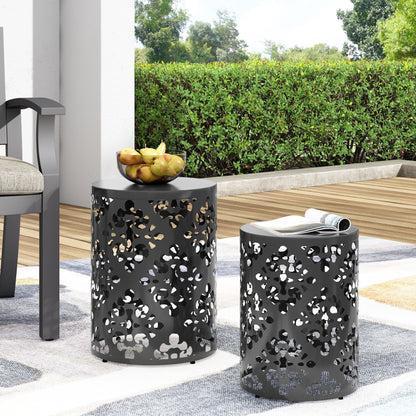Two black Outdoor Metal Modern Design End Tables with patterned tops are on a patio—one holds a bowl of pears—next to a cushioned chair and rolled magazine, set against a green hedge and wooden deck.