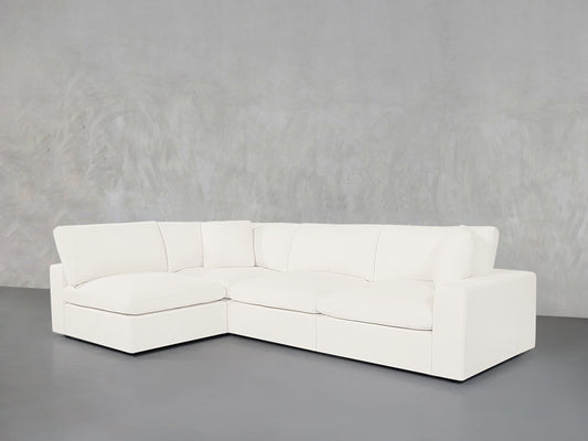 A 4-Seat Modular Open Corner Sectional with clean lines and plush cushions sits on a smooth gray floor against a textured light gray wall.