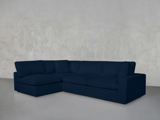 A 4-Seat Modular Open Corner Sectional with wide seats and clean lines sits against a light gray textured wall on a smooth gray floor.