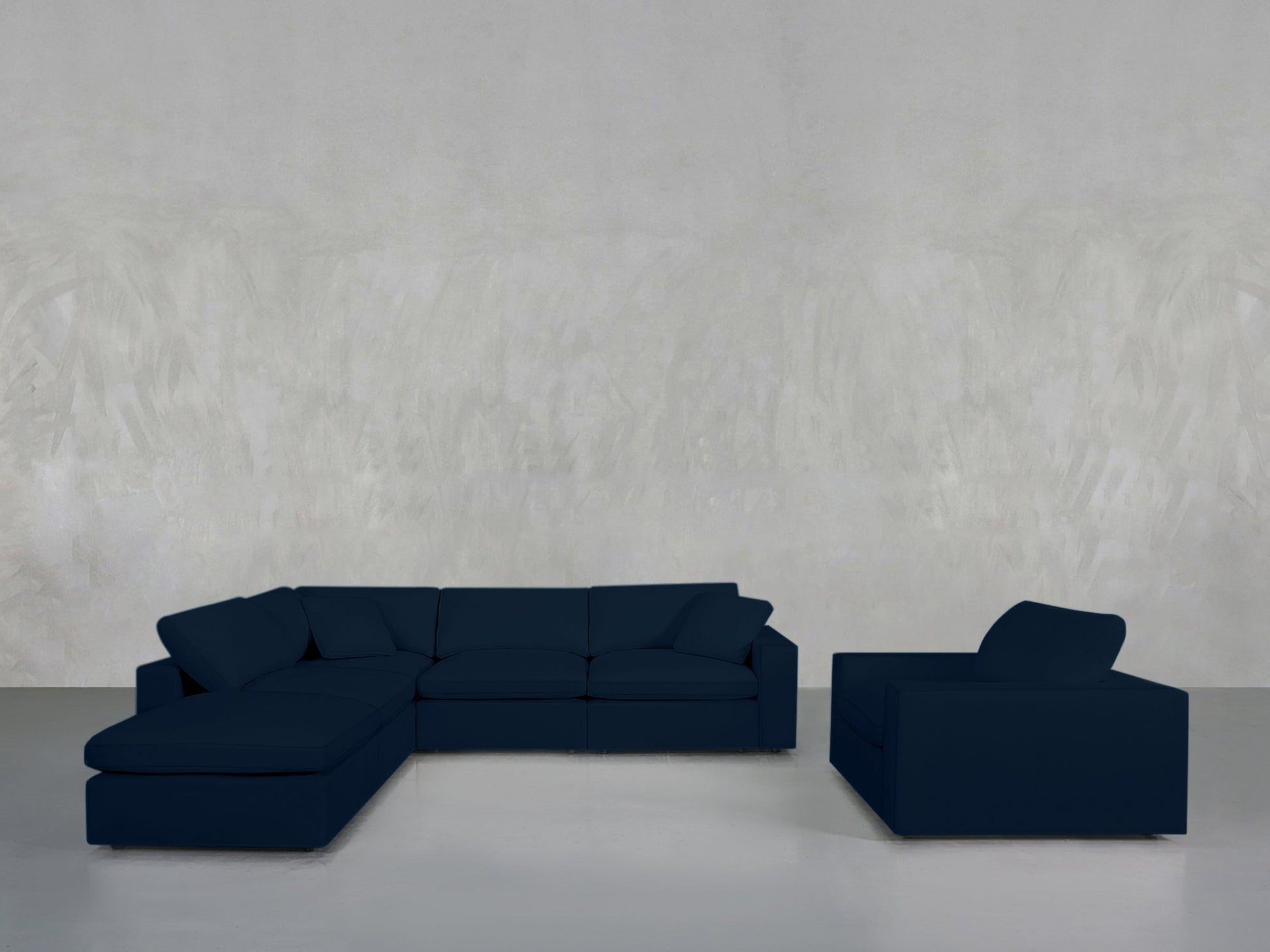The 5-1 Sectional & Armchair Set in dark blue is arranged on a light grey floor against a textured light grey wall, creating a minimalist ambiance.