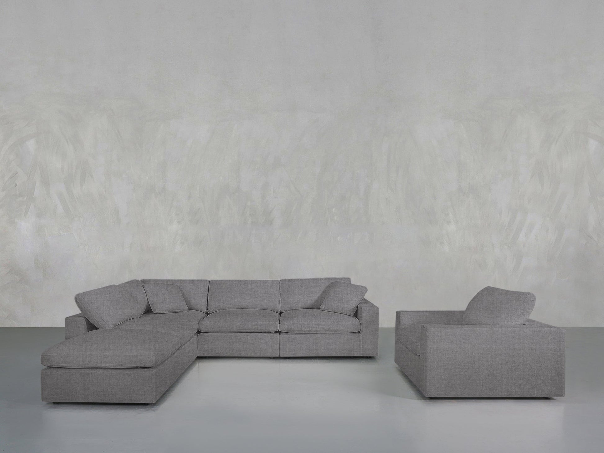 A contemporary living room showcases the 5-1 Sectional & Armchair Set in gray, with a left-side chaise lounge and a matching armchair, both placed against a simple textured gray wall.