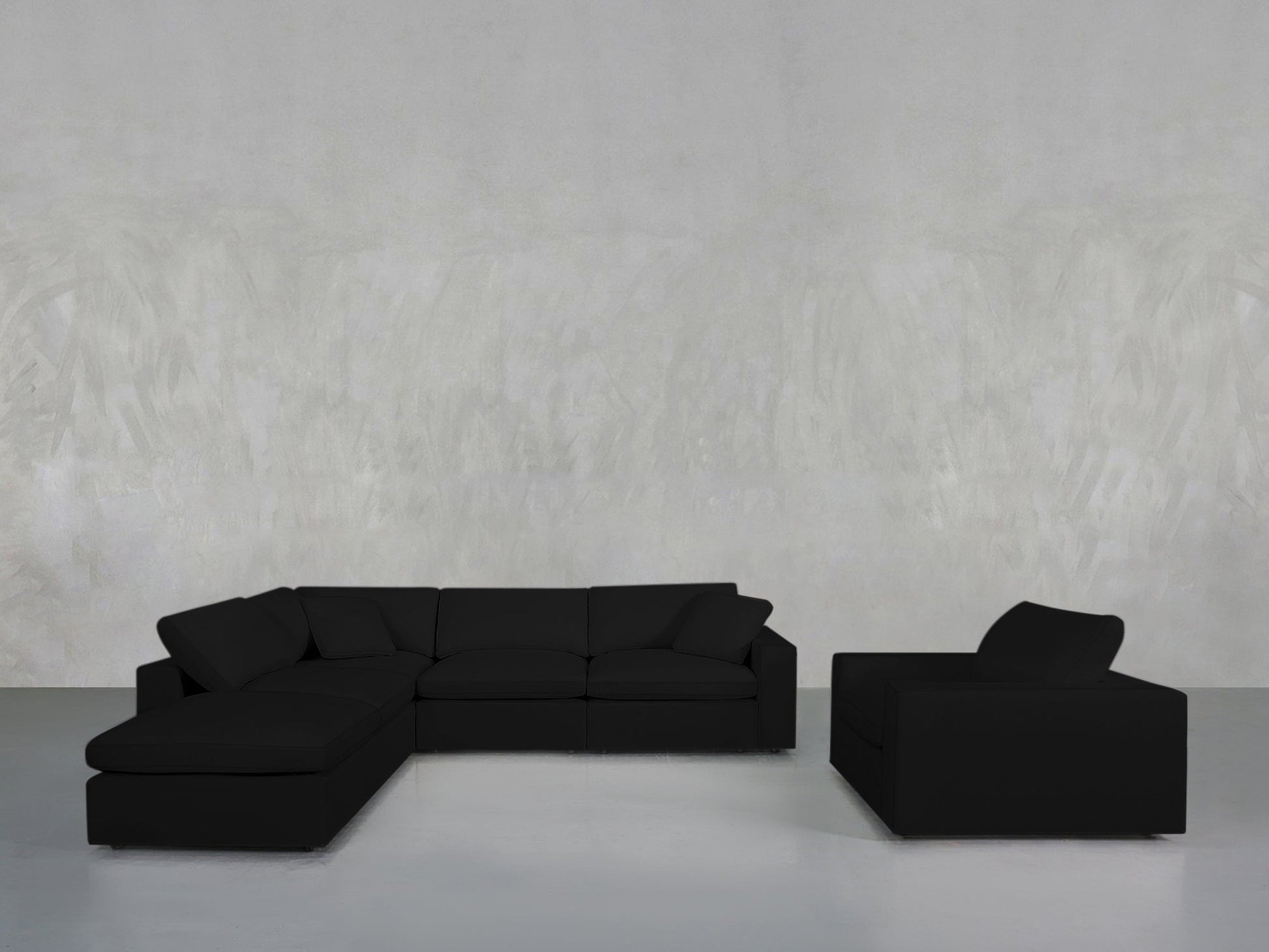 A modern living room showcases the 5-1 Sectional & Armchair Set in black, arranged against a plain light gray textured wall and a minimalist gray floor.