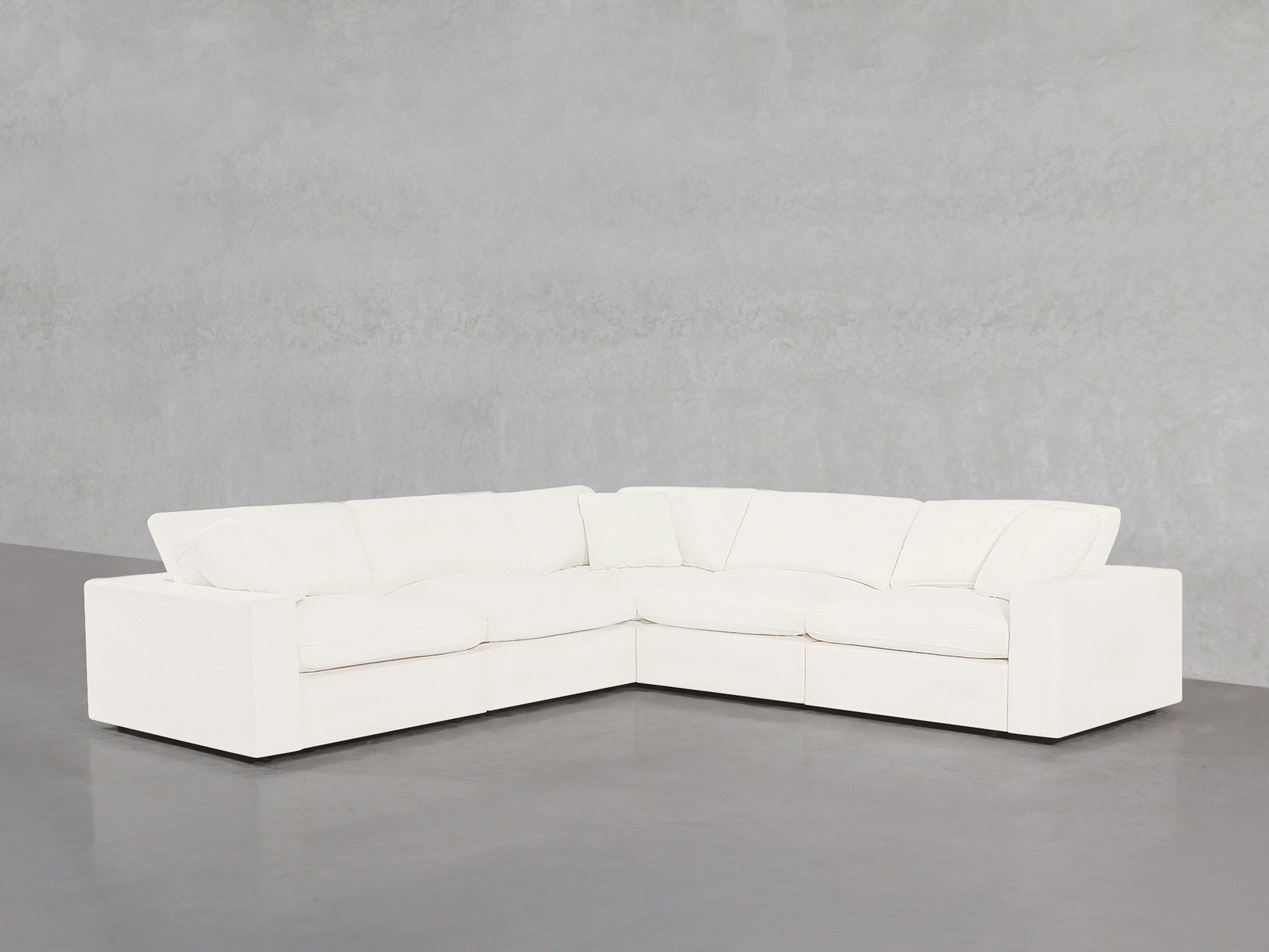 A 5-Seat Modular Corner Sectional with plush cushions is placed on a smooth gray floor against a light gray, textured wall.