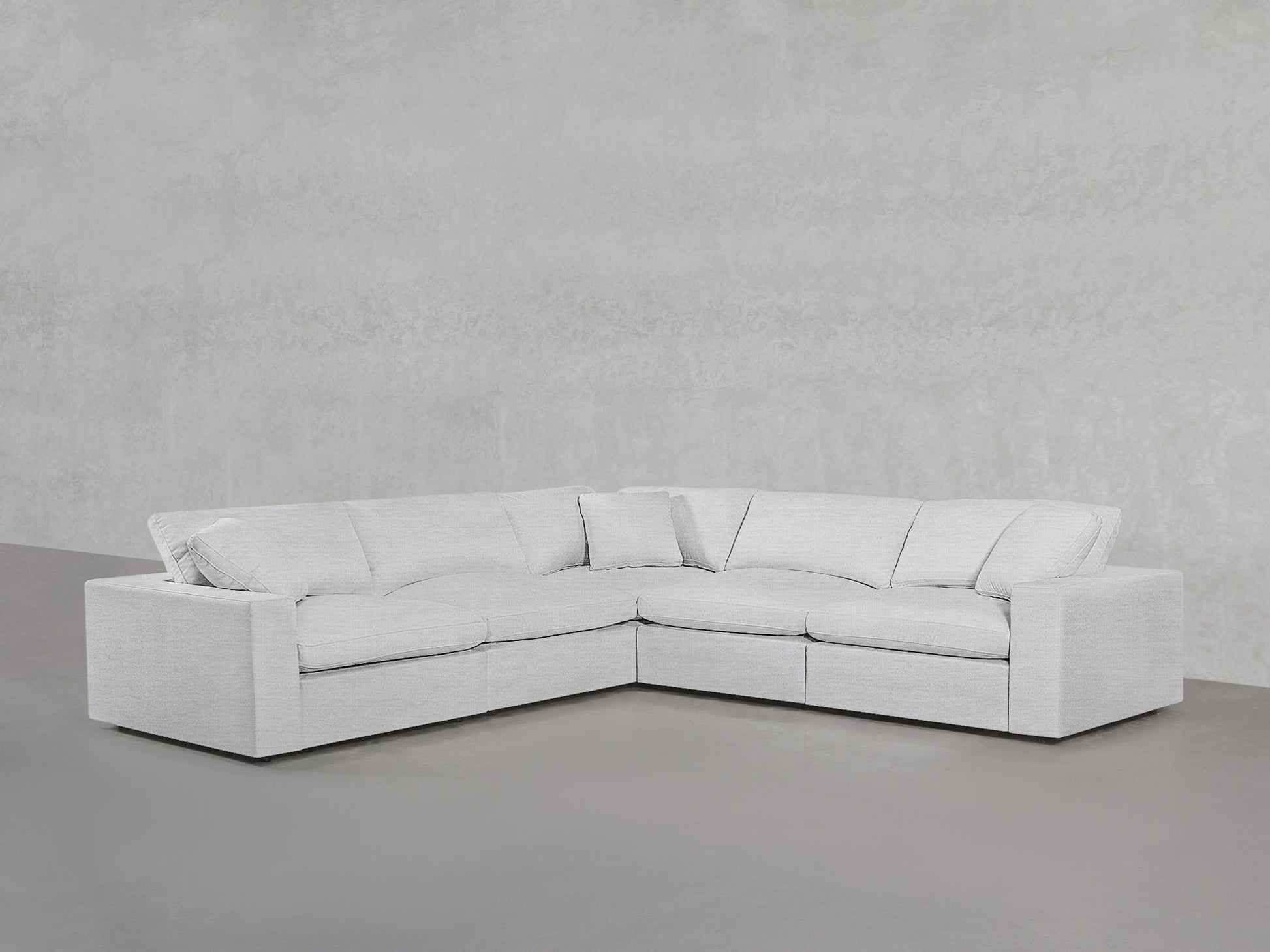 A 5-Seat Modular Corner Sectional in modern light gray with plush cushions sits against a textured light gray wall and a smooth gray floor.