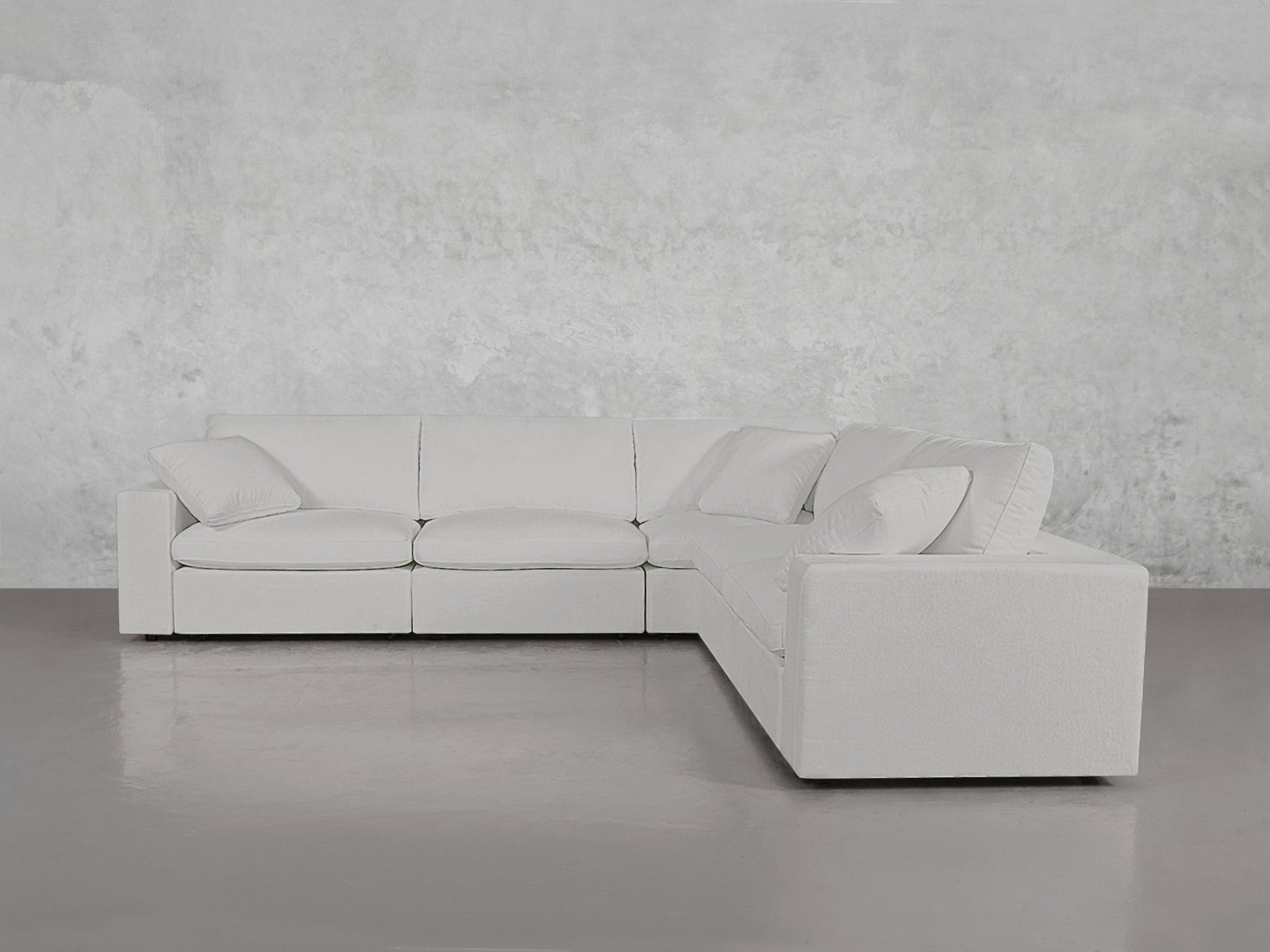 A 5-Seat Modular Corner Sectional in modern white with matching pillows sits on a gray floor against a light textured wall.