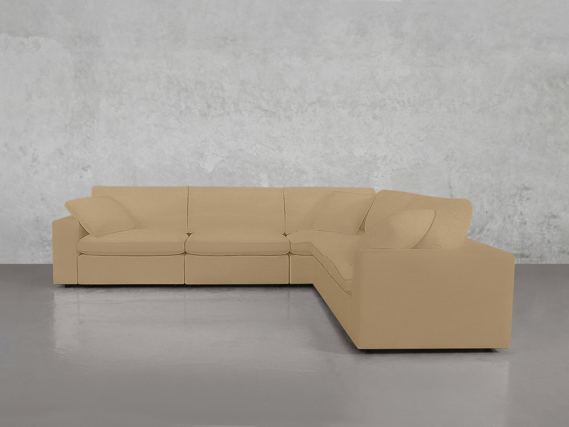 A 5-Seat Modular Corner Sectional in beige, featuring plush cushions and pillows, sits in a minimalist room with a gray polished floor and a textured light gray wall background.