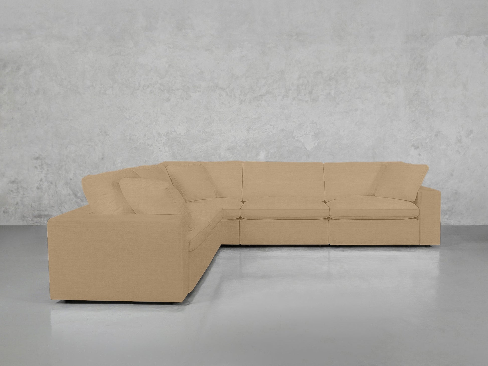 A 5-Seat Modular Corner Sectional in light beige with cushions sits on a smooth, light gray floor against a textured, light gray concrete wall.
