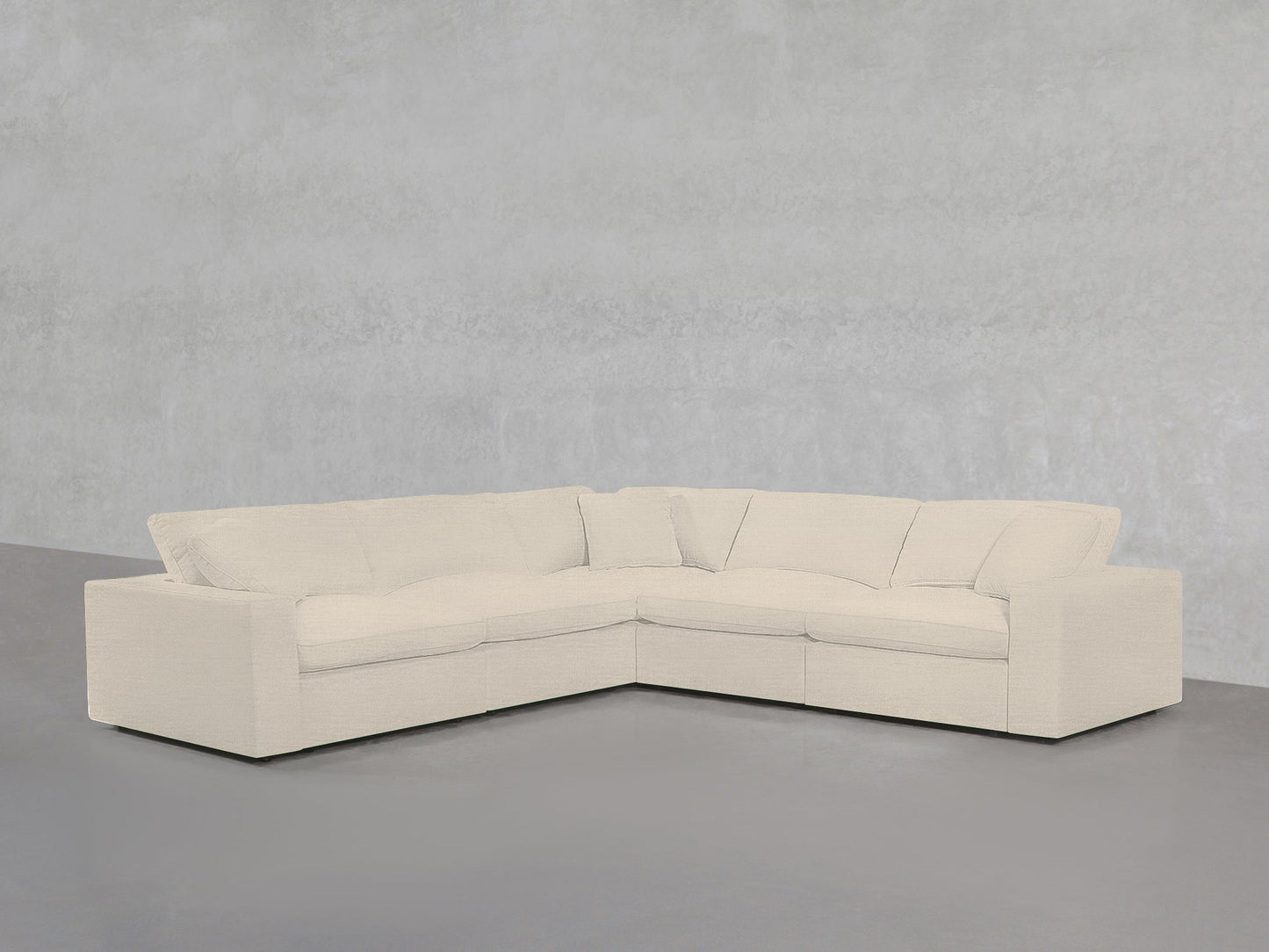 A 5-Seat Modular Corner Sectional with off-white upholstery sits against a light gray textured wall and gray floor in a minimalist room.