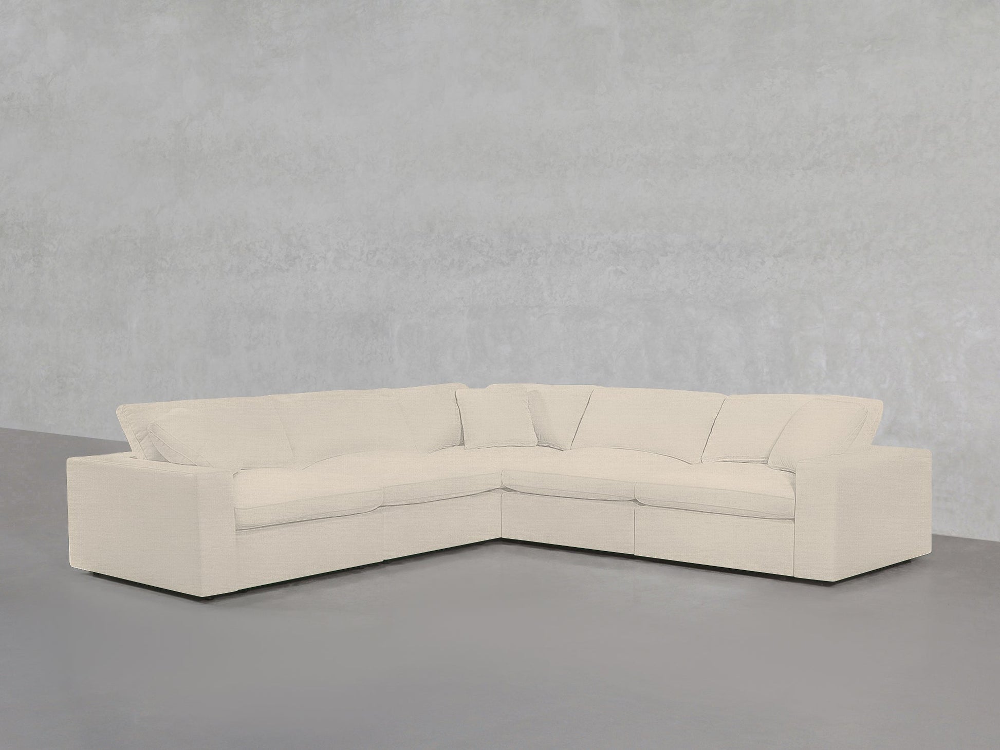 A 5-Seat Modular Corner Sectional with off-white upholstery sits against a light gray textured wall and gray floor in a minimalist room.