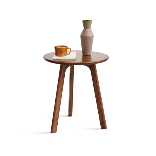 The Round Small End Table, designed for bedrooms and balconies, features a round wooden top with three angled legs, shown holding a brown ceramic mug on a white book and a tall beige vase with green-tipped opening against a white background.