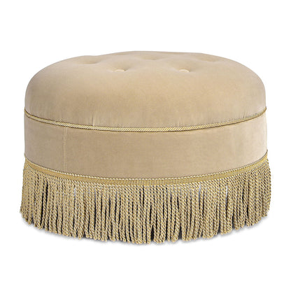 The Yolanda Round Upholstered Accent Ottoman features a smooth beige tufted top, gold braided trim, and a long gold fringed tassel skirt along the bottom edge.