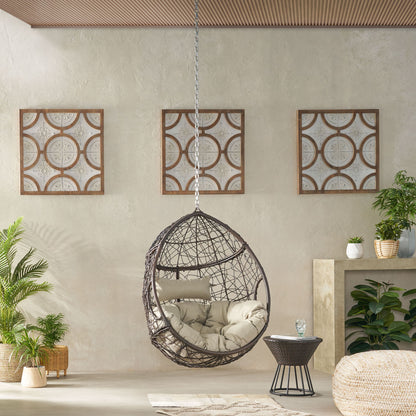 The Teardrop Hanging Chair With 8Ft Chain, featuring beige cushions, is suspended in a modern living room with geometric framed art, lush plants, a small side table, and a light-colored floor.
