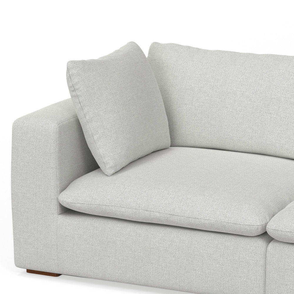A close-up of the Jasmine - Handcrafted Sofa in modern light gray fabric, featuring plush cushions and a square armrest, set against a white background.
