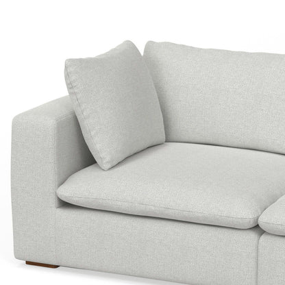A close-up of the Jasmine - Handcrafted Sofa in modern light gray fabric, featuring plush cushions and a square armrest, set against a white background.
