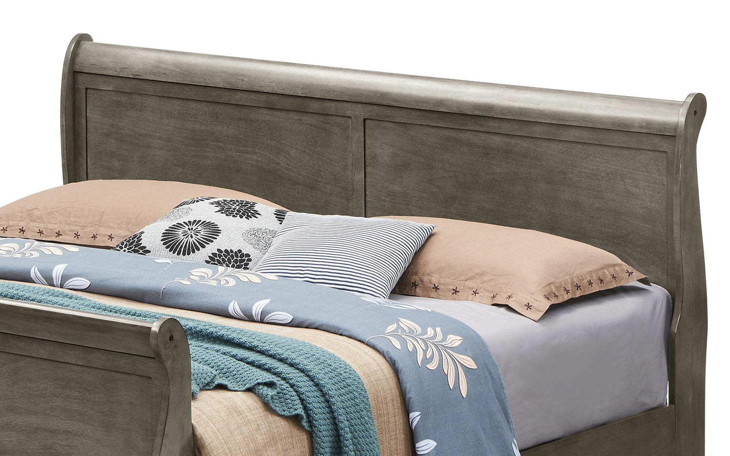 The Panel Sleigh Bed features a curved headboard and footboard and is styled with tan pillows, patterned throw pillows, a light blue floral blanket, and a green knitted throw against a plain white background.