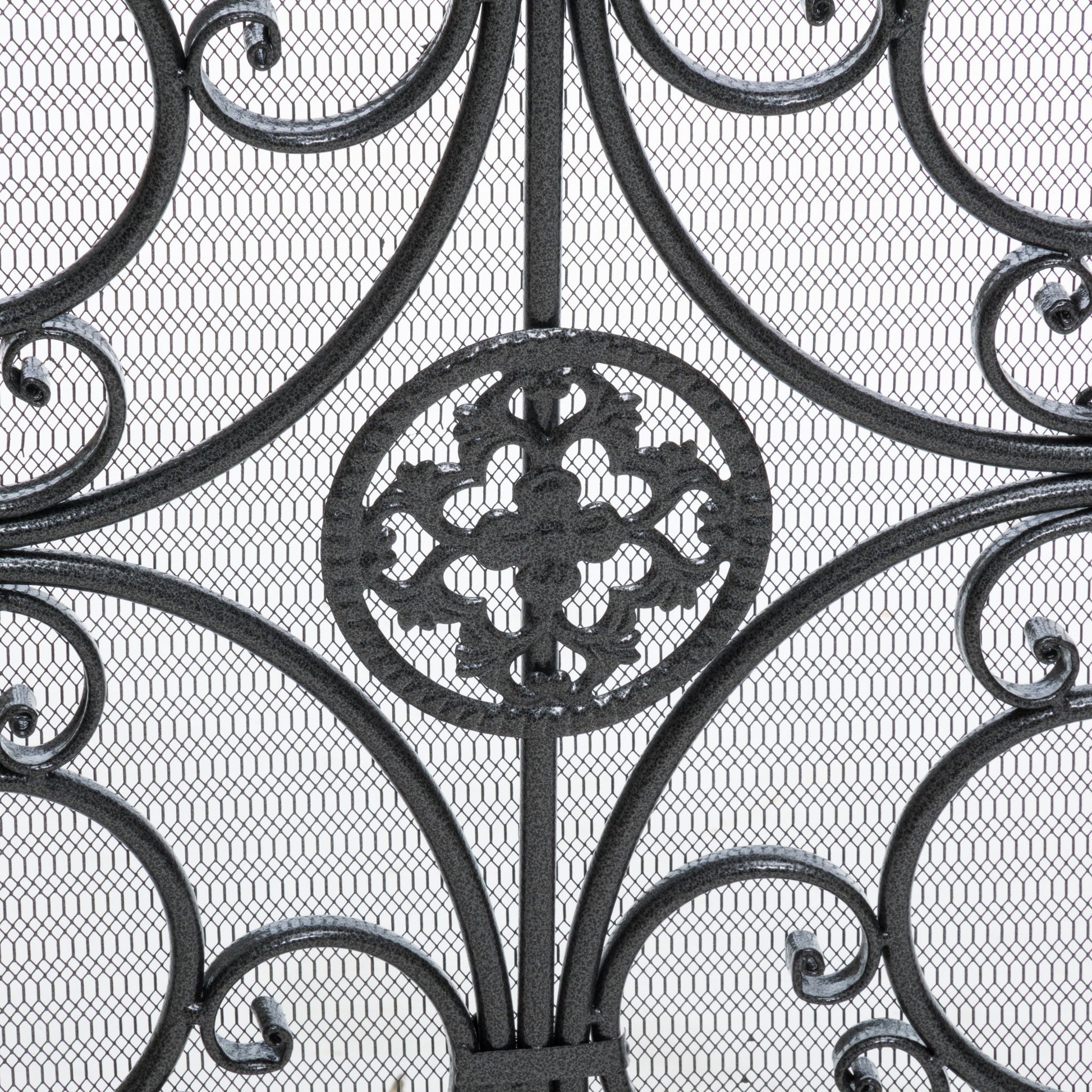 Close-up of the Darcie Wrought Fireplace Screen showcasing an ornate circular floral centerpiece with swirling curves and symmetrical details, set against a fine metal mesh background.