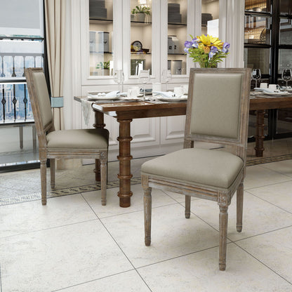 Two Traditional Style Dining Chairs With Fabric Upholstery and wooden frames sit near a set dining table with plates and glasses. The room has tiled floors, large windows, cabinets, and a vase of flowers on the table.
