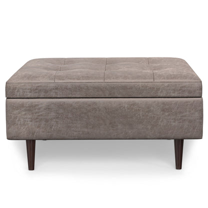 The Shay Large Square Coffee Table Storage Ottoman features light brown upholstery, subtle tufted top detailing, and four dark wooden legs in a mid-century style, displayed against a white background.