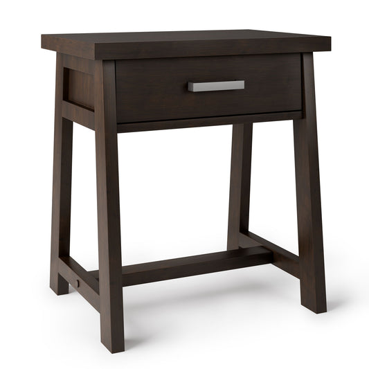 The Sawhorse - Handcrafted Bedside Table is a dark brown wooden nightstand with a central drawer, silver handle, and four legs connected by horizontal supports near the base.