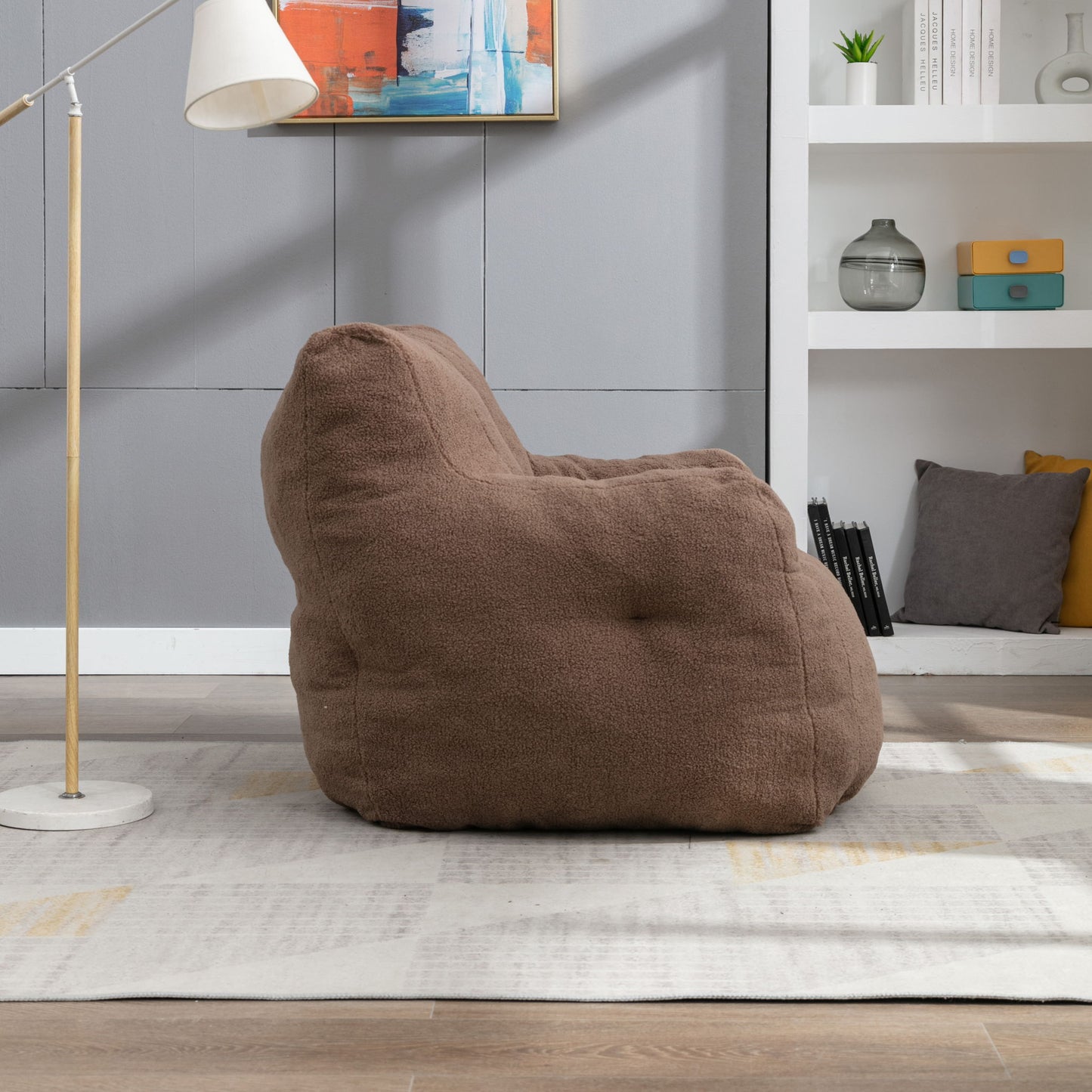 A Soft Teddy Fabric Tufted Foam Bean Bag Chair sits on a light rug in a modern living room, with a floor lamp, shelves with decor, and abstract art on the wall in the background.