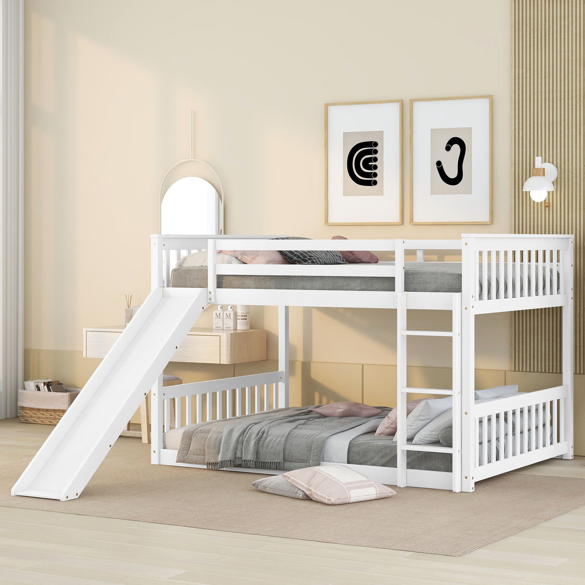 A children's bedroom featuring the Bunk Bed With Slide And Ladder in white, with two stacked beds, pillows and bedding on top, cushions below, light-colored walls, framed art, and a mirror.