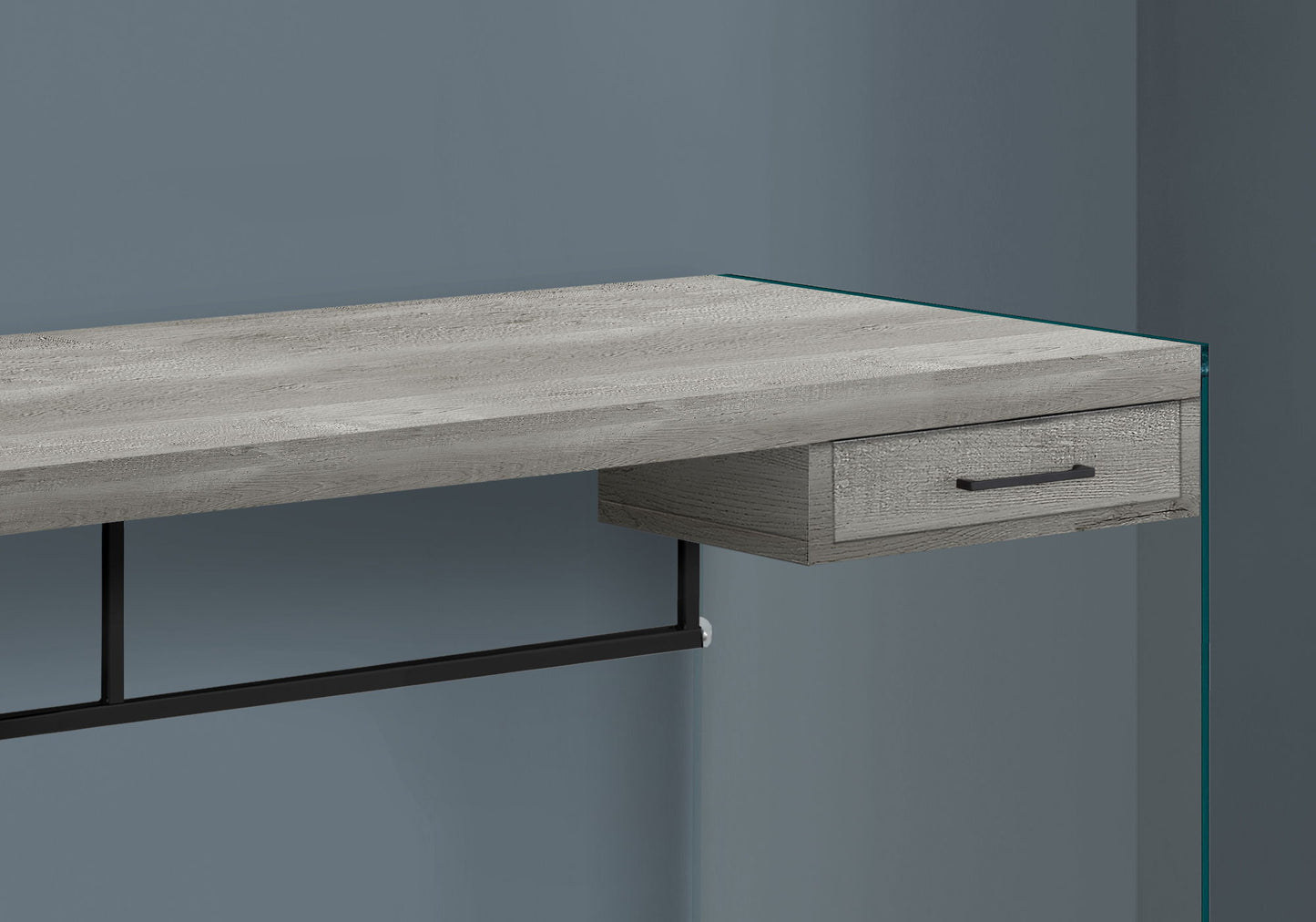 The Contemporary Design Computer Desk For Home Office features a light gray wood finish, single storage drawer with black handle, black metal support, and a glass side panel, shown against a blue-gray wall.