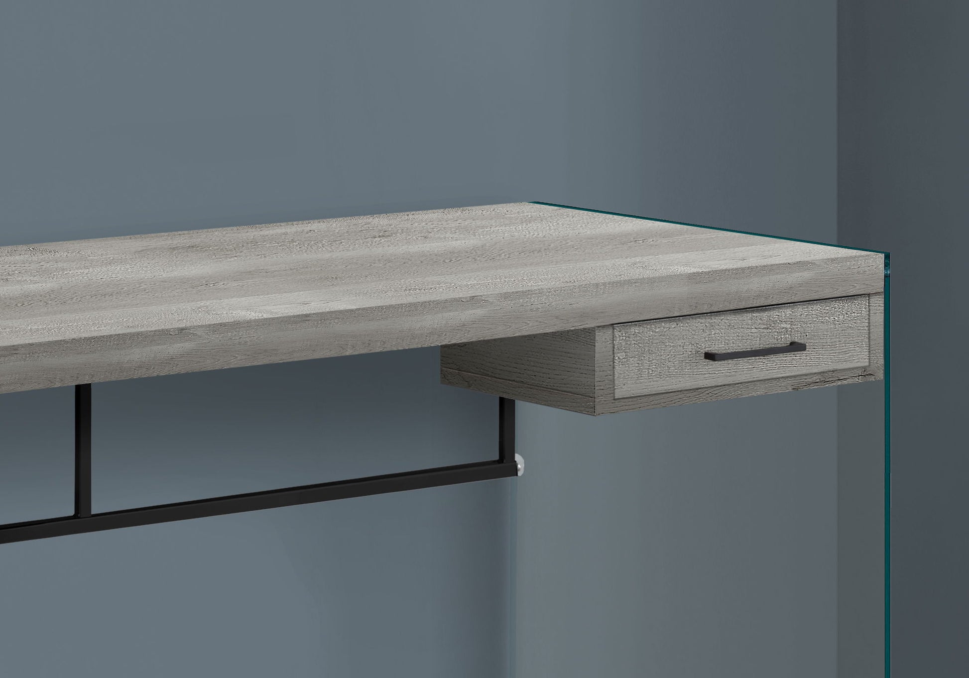 The Contemporary Design Computer Desk For Home Office features a light gray wood finish, single storage drawer with black handle, black metal support, and a glass side panel, shown against a blue-gray wall.