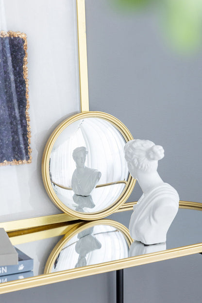 A white bust sits on a glass table with a gold rim, reflecting in the Round Mirror—Circle Mirror With Iron Frame—for living room, bedroom, vanity, entryway, or hallway. Modern wall art decorates the gray wall in the background.