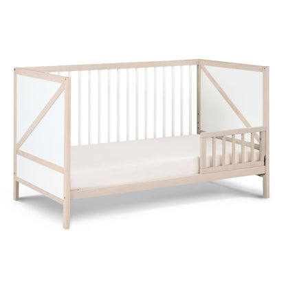 The Pixie Zen 3-in-1 Crib in Walnut features white panel accents, open slatted sides, and a partial safety rail on one side, displayed against a white background.