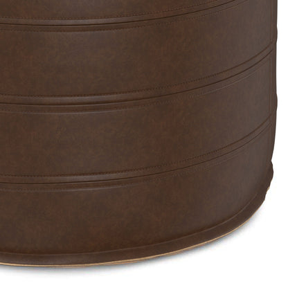 Close-up view of the Brody - Round Pouf, a brown, cylindrical seat featuring visible stitched horizontal seams. Upholstered in leather or faux leather with a smooth, subtly textured surface.