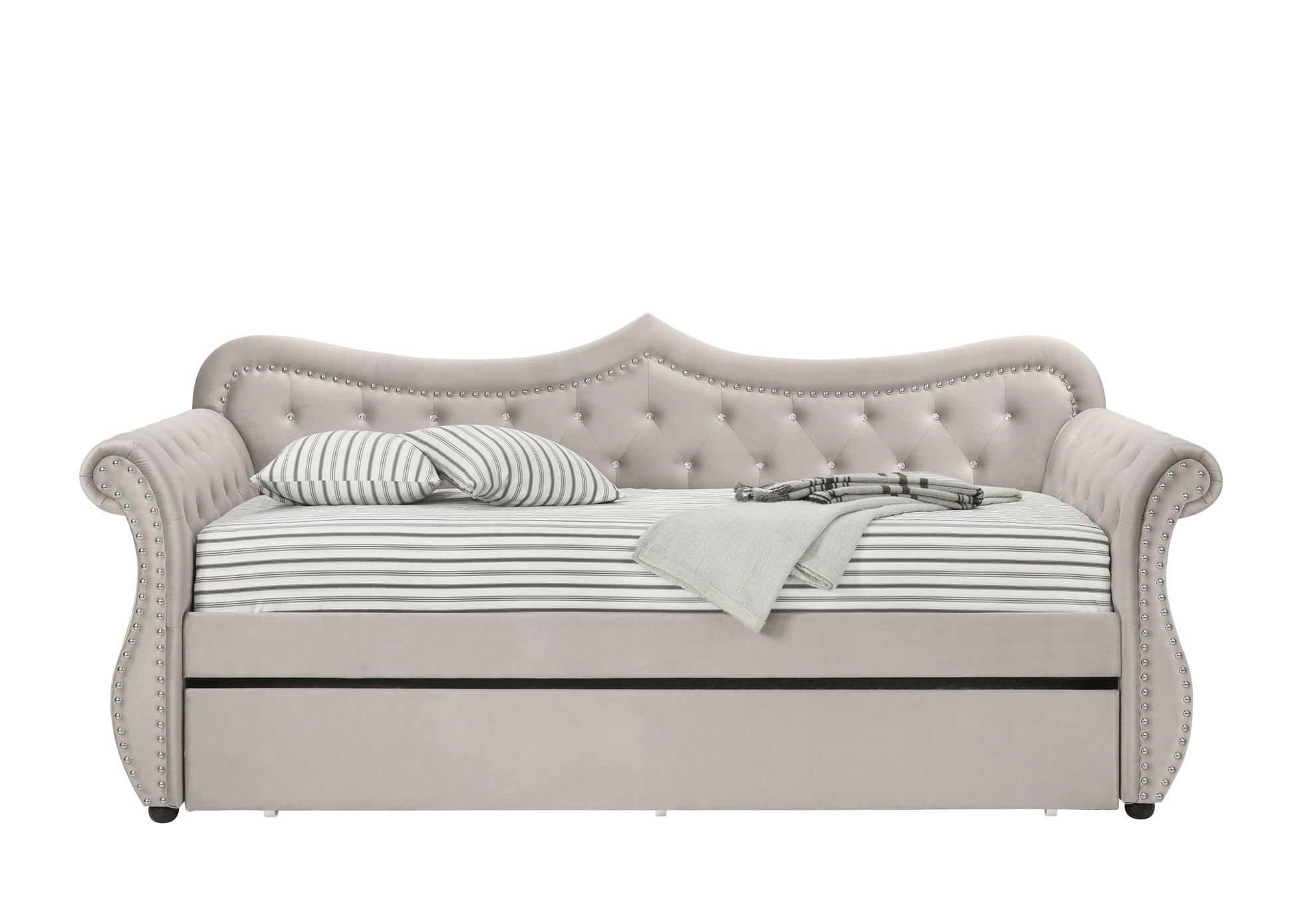The Adkins - Twin Daybed With Trundle - Beige features an elegant upholstered design with a tufted backrest and arms, striped mattress and pillows, a folded gray blanket, a book, and a pull-out trundle bed underneath.
