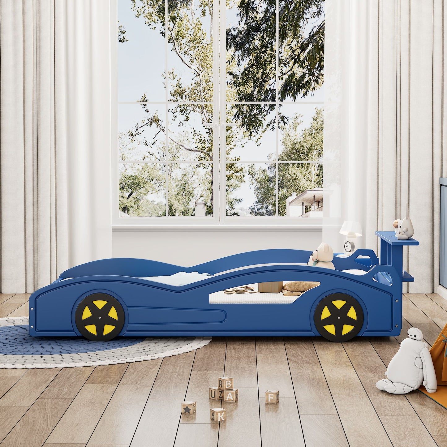 A Wooden Race Car Bed, Car Shaped Platform Twin Bed With Wheels For Teens, stands in a bright children's room with stuffed animals, letter blocks, large windows with white curtains showing trees, and a round rug completing the cozy look.
