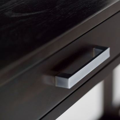 Close-up of the Kitchener - Handcrafted Table, highlighting its dark wood grain and a sleek, modern rectangular metallic drawer handle.
