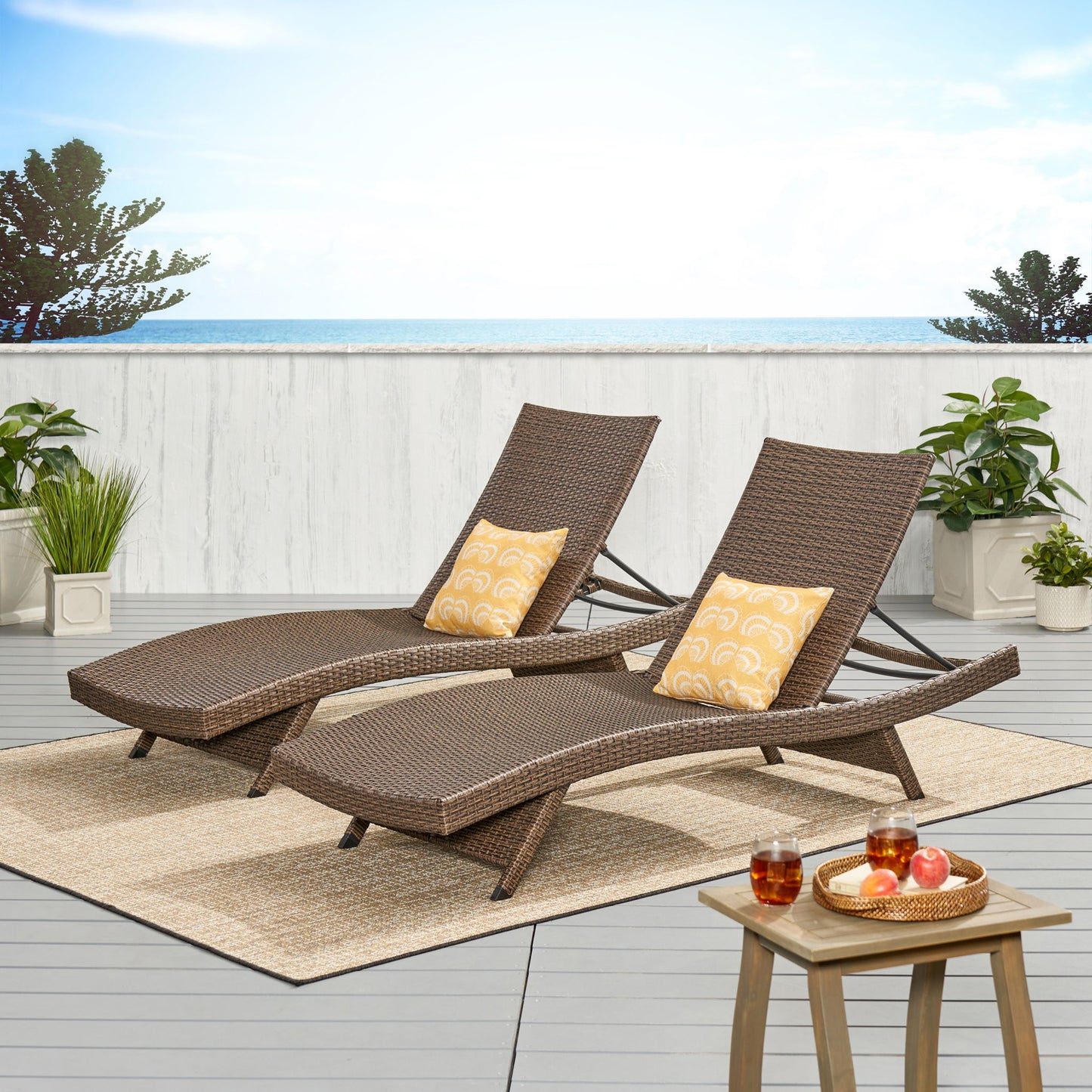 Two Salem - Chaise Lounge chairs with yellow patterned pillows are on a seaside deck with potted plants. A small table holds drinks and fruit, creating a bright, peaceful, and inviting outdoor setting.