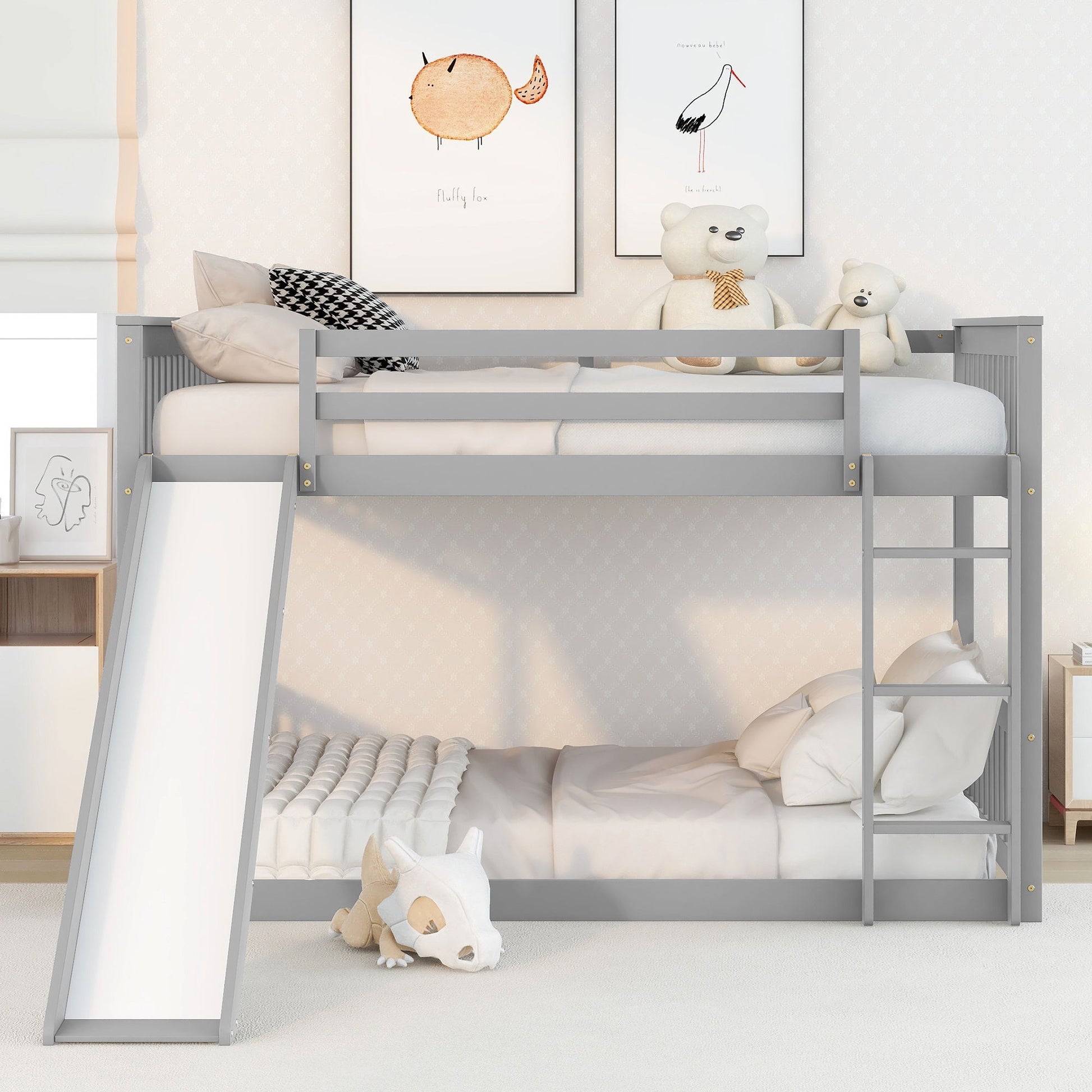 A modern kids' room featuring the Bunk Bed With Slide And Ladder in gray, with stuffed toys and pillows on the top bunk, white bedding below, wall art, and a plush animal toy completing the decor.